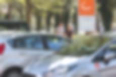 cambio-Station mit zwei cambio-Autos im Vordergrund und zwei Menschen im Hintergrund.