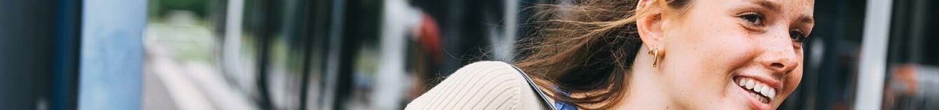 Junge Frau steht fröhlich an einer Haltestelle und bewegt sich zur einfahrenden Vamos-StadtBahn.