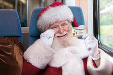 Weihnachtsmann in der Bahn hält fröhlich schauend ein Deutschlandticket hoch.