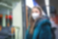 Eine Frau mit FFP2-Maske wartet in einer StadtBahn-Haltestelle. Im Hintergrund ist eine Vamos-Bahn zu sehen.
