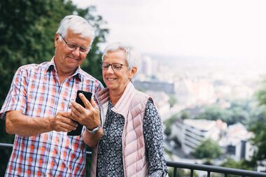 Ein älteres Paar blickt lächelnd gemeinsam auf ein Handy.
