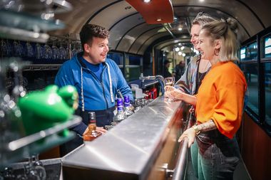 Zwei Frauen unterhalten sich im SparrenExpress mit dem Barkeeper.