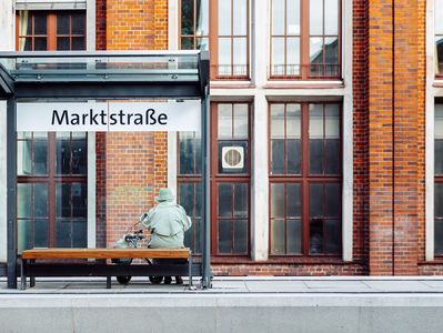 Dame mit Rollator sitzt an der Haltestelle Marktstraße.