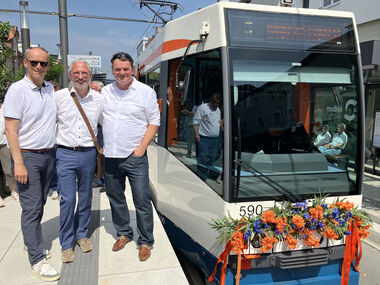 Martin Uekmann, Bezirksbürgermeister Jesco von Kuczkoswki und Martin Adamski stehen fröhlich am neuen Hochbahnsteig in Brackwede neben einer mit Blumen geschmückten StadtBahn.