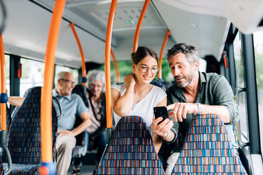 Ein Mann und eine Frau sitzen im Bus und schauen auf ein Smartphone.