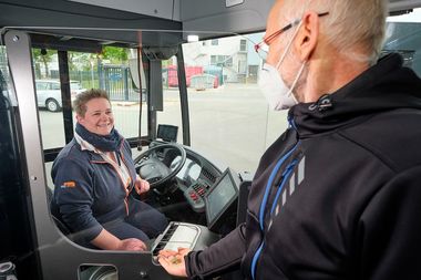 Auf dem Bild ist eine moBiel Bus-Fahrerin auf ihrem Fahrersitz zu sehen. Ein Fahrgast möchte ein Ticket kaufen. Zwischen ihnen sieht man die Trennscheibe aus Plexiglas, die beide vor der Ansteckung mit dem Coronavirus schützen soll.