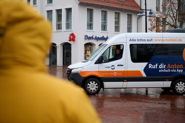 Mit meinAnton kommst du bei jedem Wetter an dein Ziel. Person im Regenmantel im Vordergrund, meinAnton-Fahrzeug im Hintergrund.