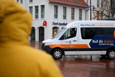 Mit meinAnton kommst du bei jedem Wetter an dein Ziel. Mit meinAnton kommst du bei jedem Wetter an dein Ziel. Person im Regenmantel im Vordergrund, meinAnton-Fahrzeug im Hintergrund.