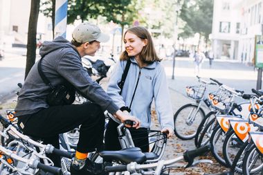 Ein P&auml;rchen unterh&auml;lt sich an Fahrradst&auml;ndern in der Stadt. Im Hintergrund sind Fahrr&auml;der von meinSiggi zu sehen.