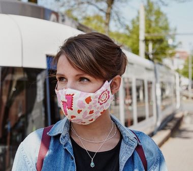 Frau mit Mund-Nasen-Schutz vor einer StadtBahn.