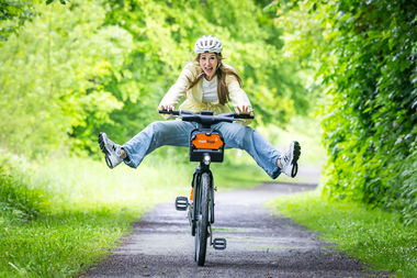Eine Frau f&auml;hrt mit einem Fahrrad von meinSiggi durch eine Pf&uuml;tze und hebt dabei freudig die Beine an.