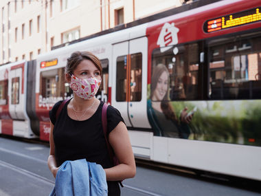 Frau mit Mund-Nasen-Schutz vor einer StadtBahn.